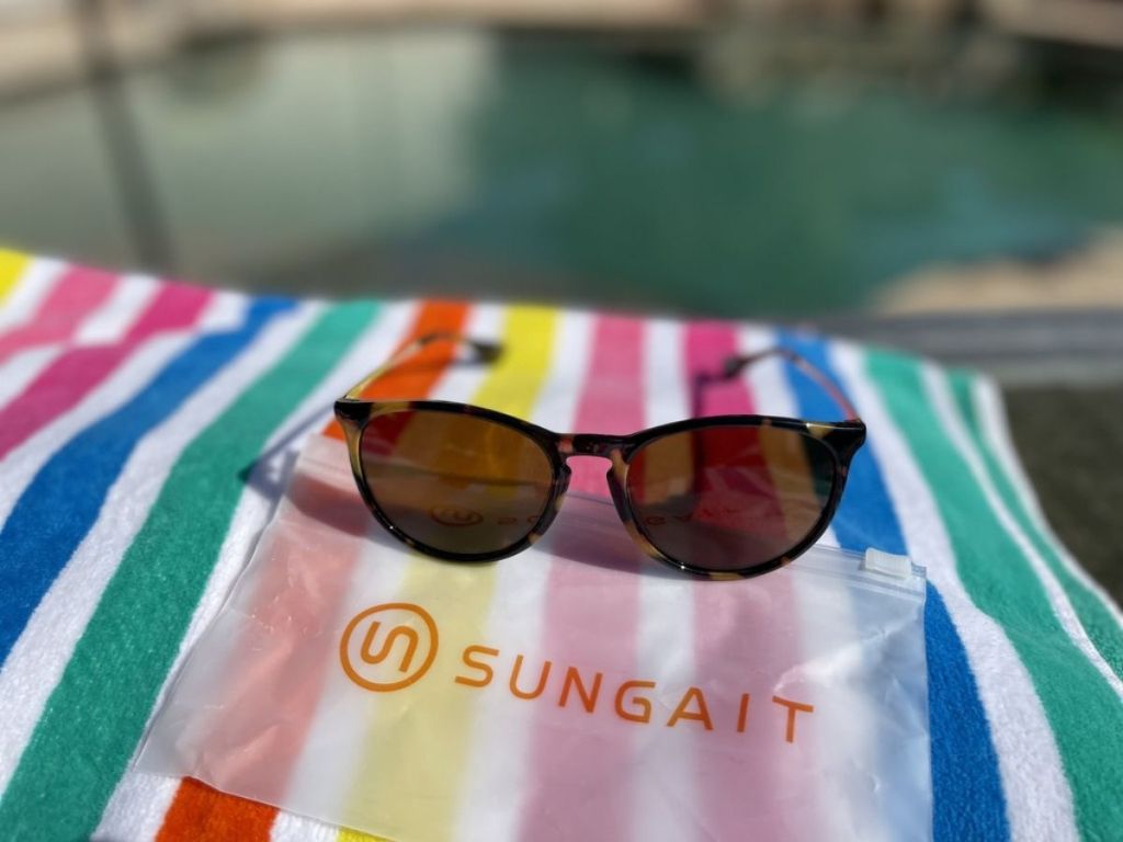 sunglasses resting on Sungait bag on top of multicolored striped beach towel