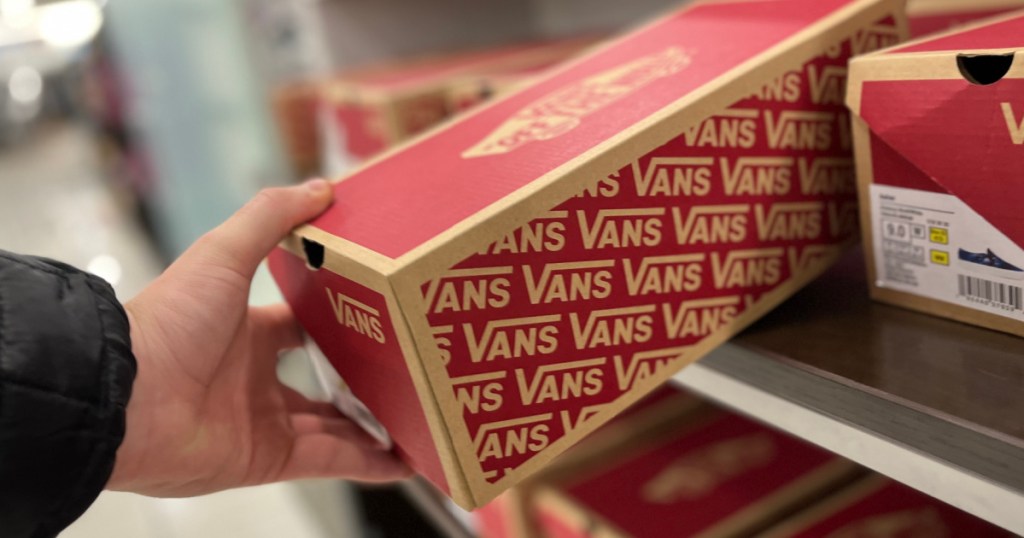 hand grabbing shoebox labeled "vans" off store shelf