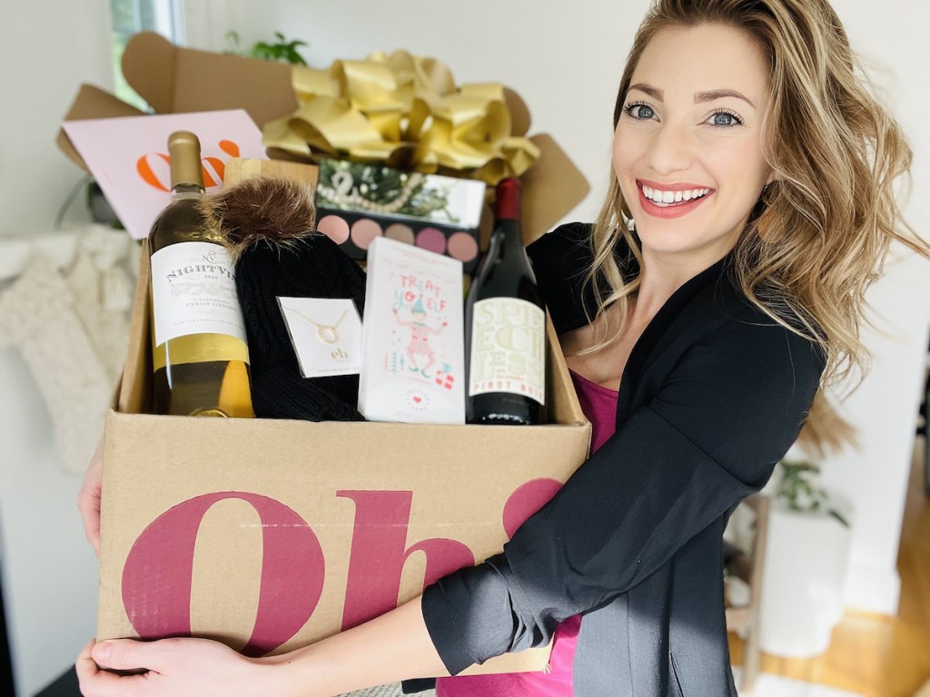 woman holding box full of wine and other holiday goodies