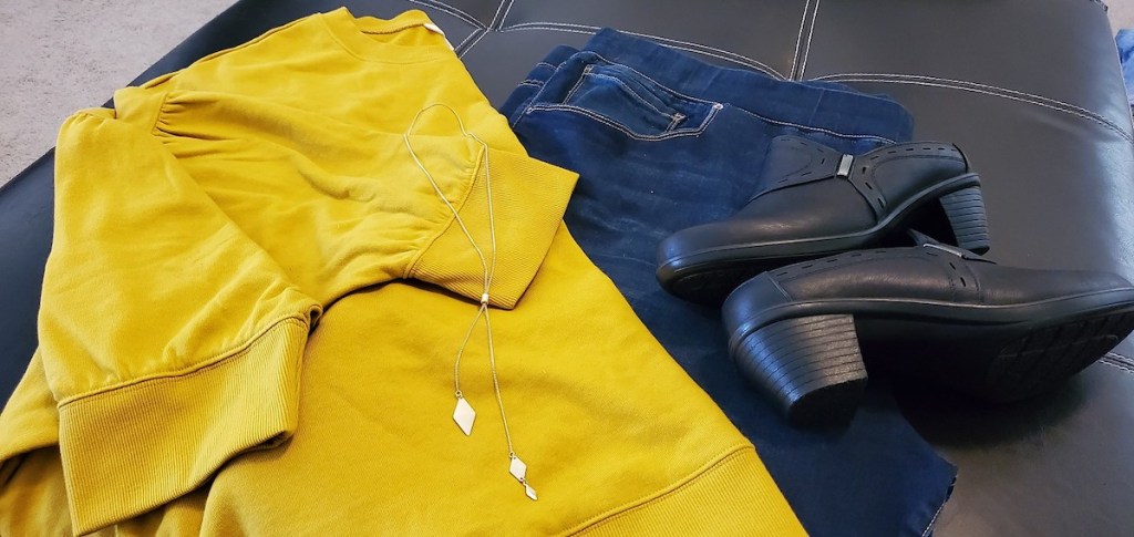 yellow sweater shirt jeans gold necklace and black boots laying on table