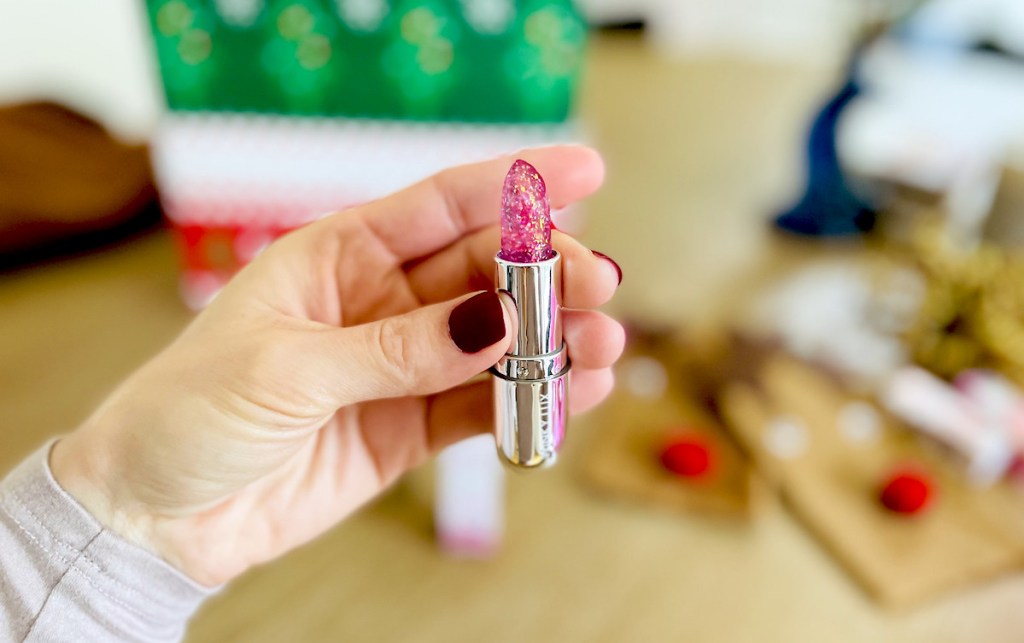 hand holding glittery lipstick in front of christmas stuff