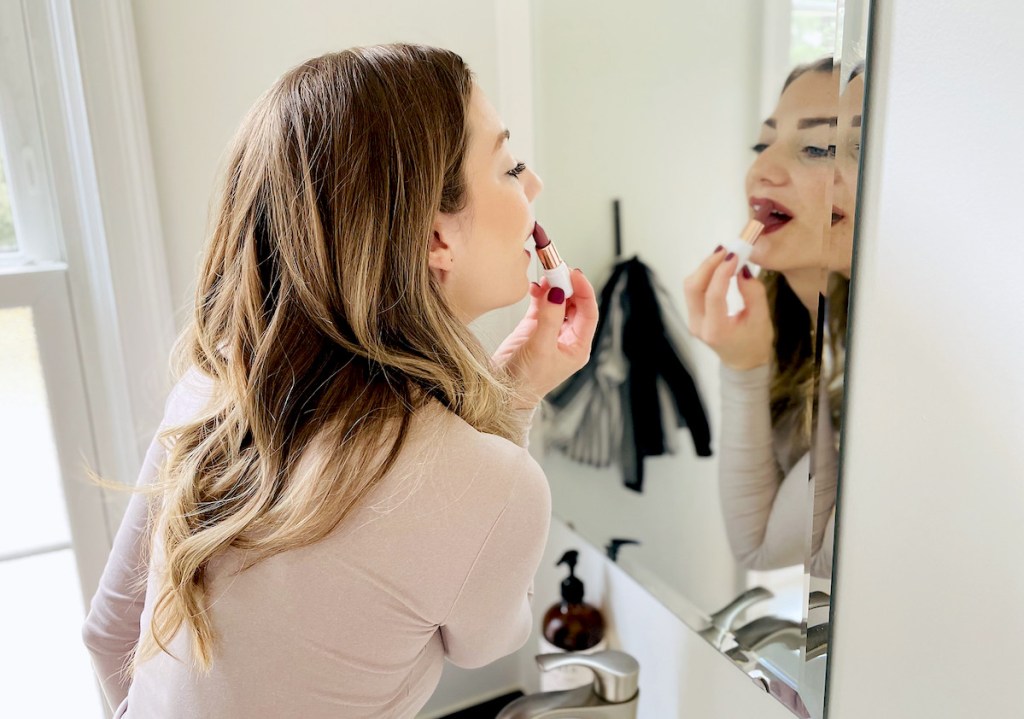 woman looking in mirror putting on lipstick