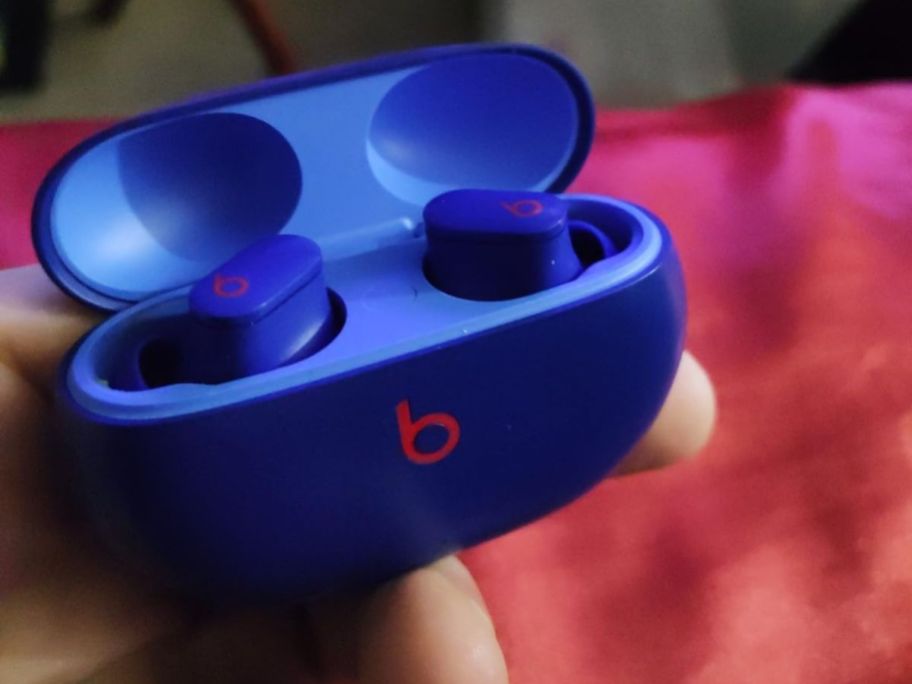Hand holding a pair of Beats Studio Buds in their charging case