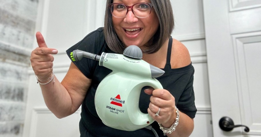 woman smiling and holding a green and grey Bissell hand steamer tool and pointing to