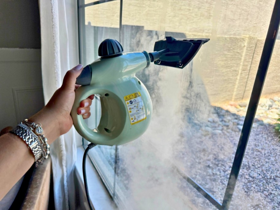 hand using a green Bissell SteamShot to clean a window