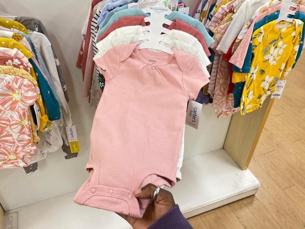 hand holding girls carter's baby bodysuits in store