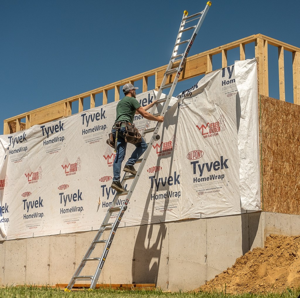Man standing on a ladder leaning against a house being built