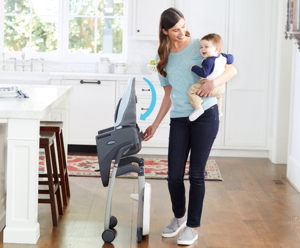Woman holding a baby while folding up a highchair