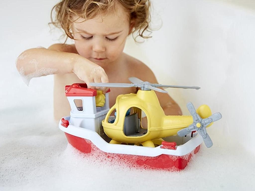 child playing with green toys boat and helicopter in bath tub
