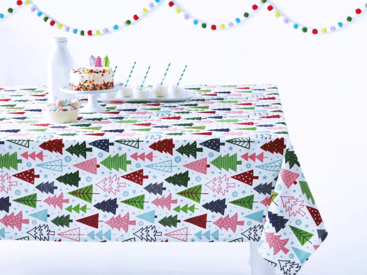 Christmas tablecloth with brightly colored Christmas tree pattern on a table set with milk and Christmas cookies.