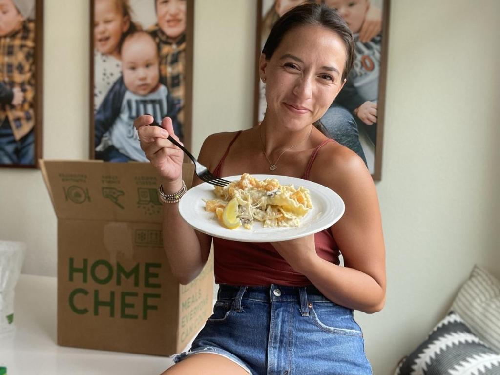 woman holding a plate of food next to a Home Chef box