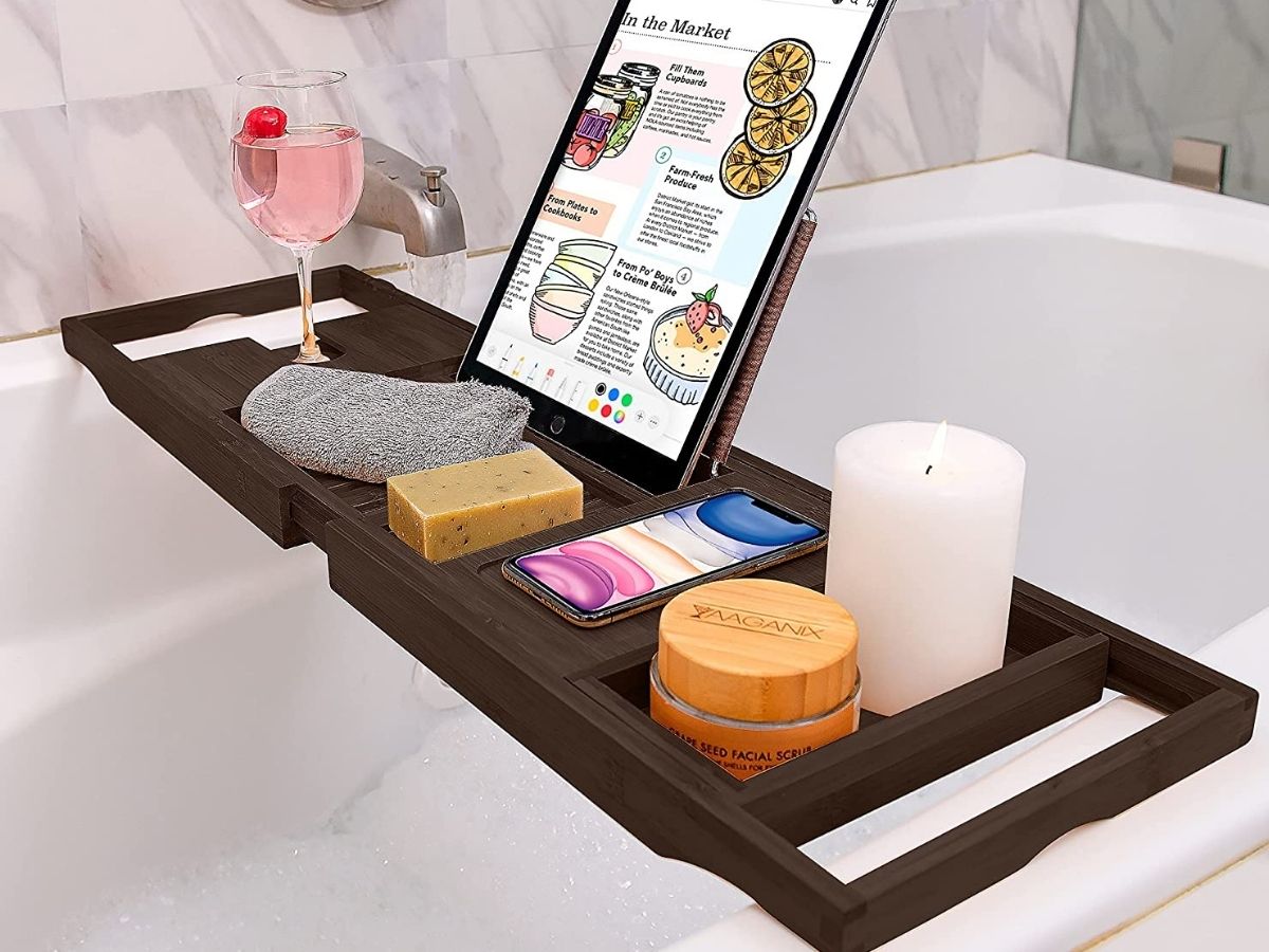 brown bamboo bathtub tray holding drink, tablet, soap, phone and candle