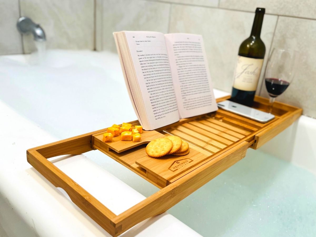  bamboo bathtub tray holding drink, wine bottle, book, cheese, and crackers