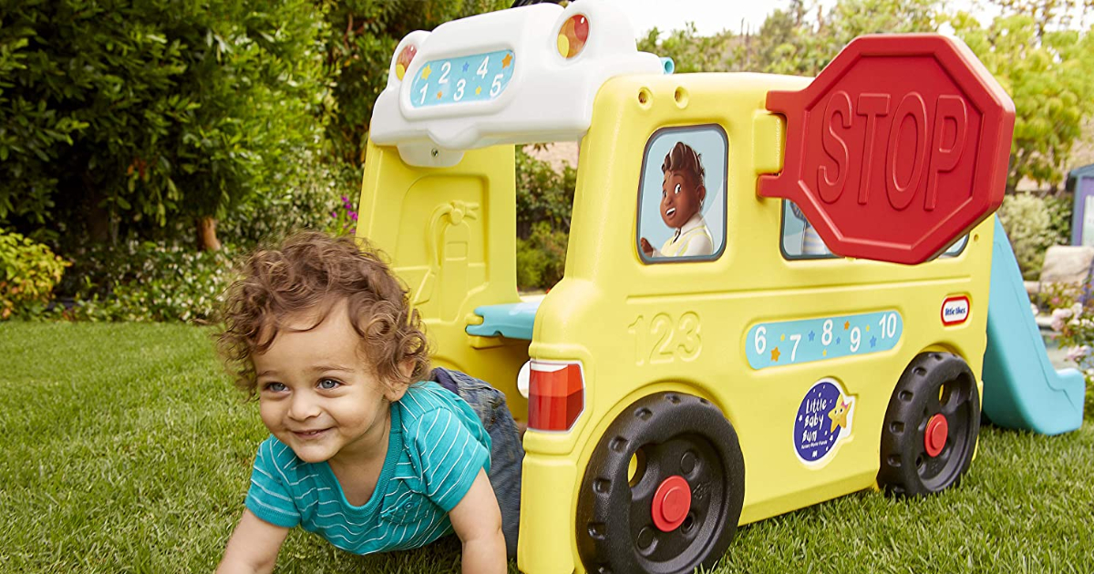young child crawling out of the Little Tikes Little Baby Bum Bus playset while outdoors near trees