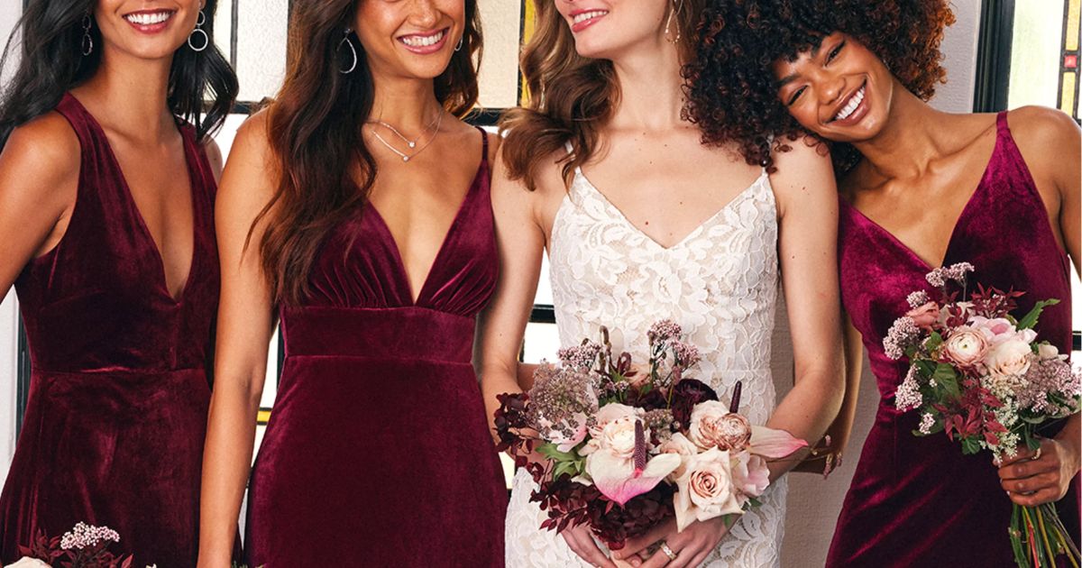 a bride in a white lace dress flanked by3 bridesmaids in wine colored dresses 