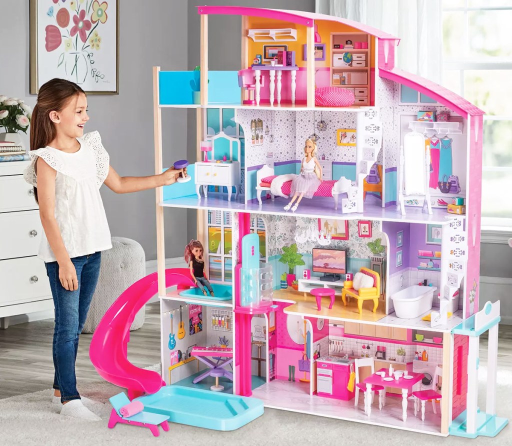 girl standing next to huge dollhouse