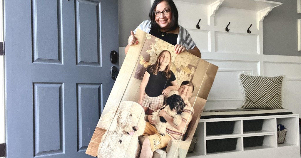 woman holding large photo of kids an dogs on wood pallet board in entryway of house