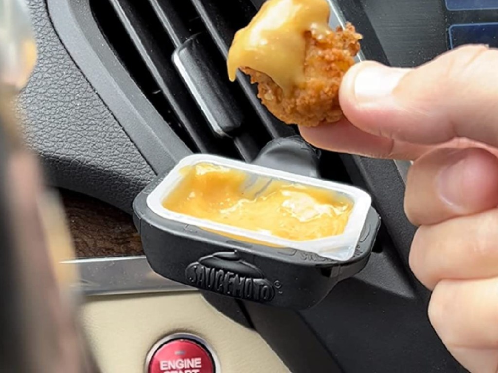 person dipping chicken nugget into sauce in container in car