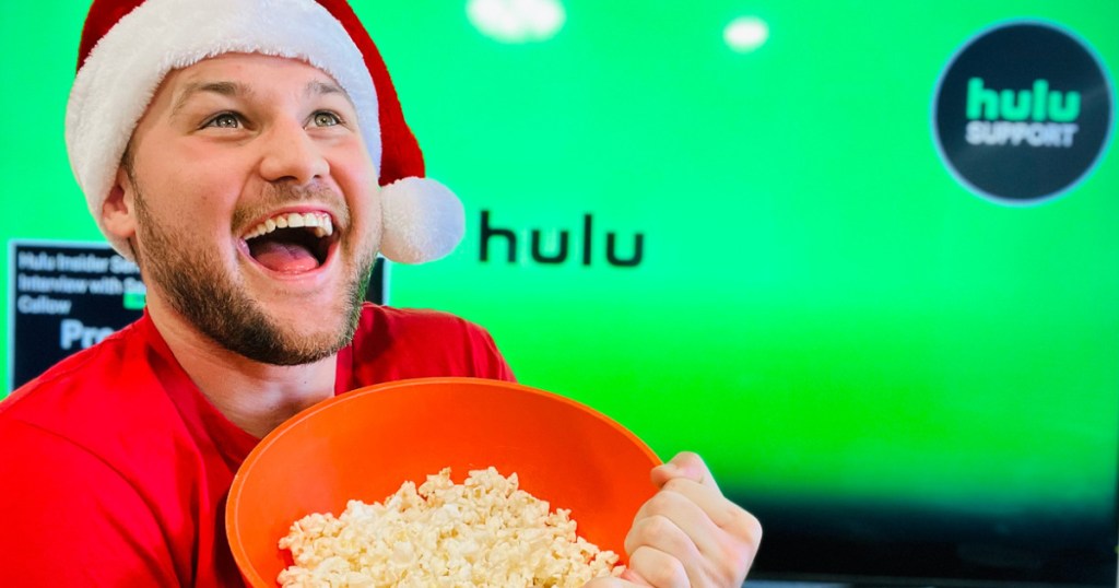man in santa hat holding bowl of popcorn in front of tv