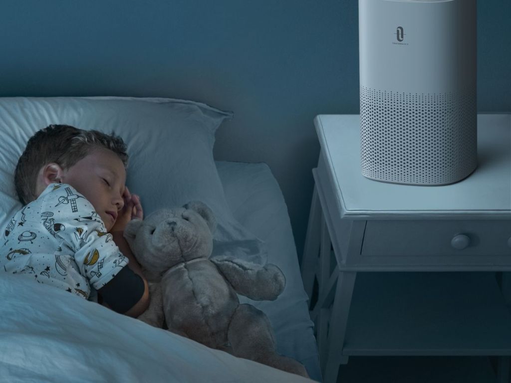 boy sleeping in bed next to air purifier