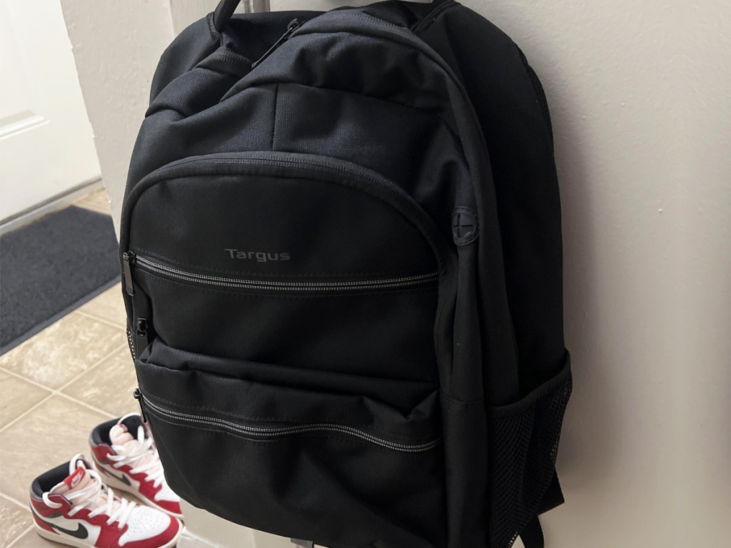 black laptop backpack hanging on wall near pair of nike shoes