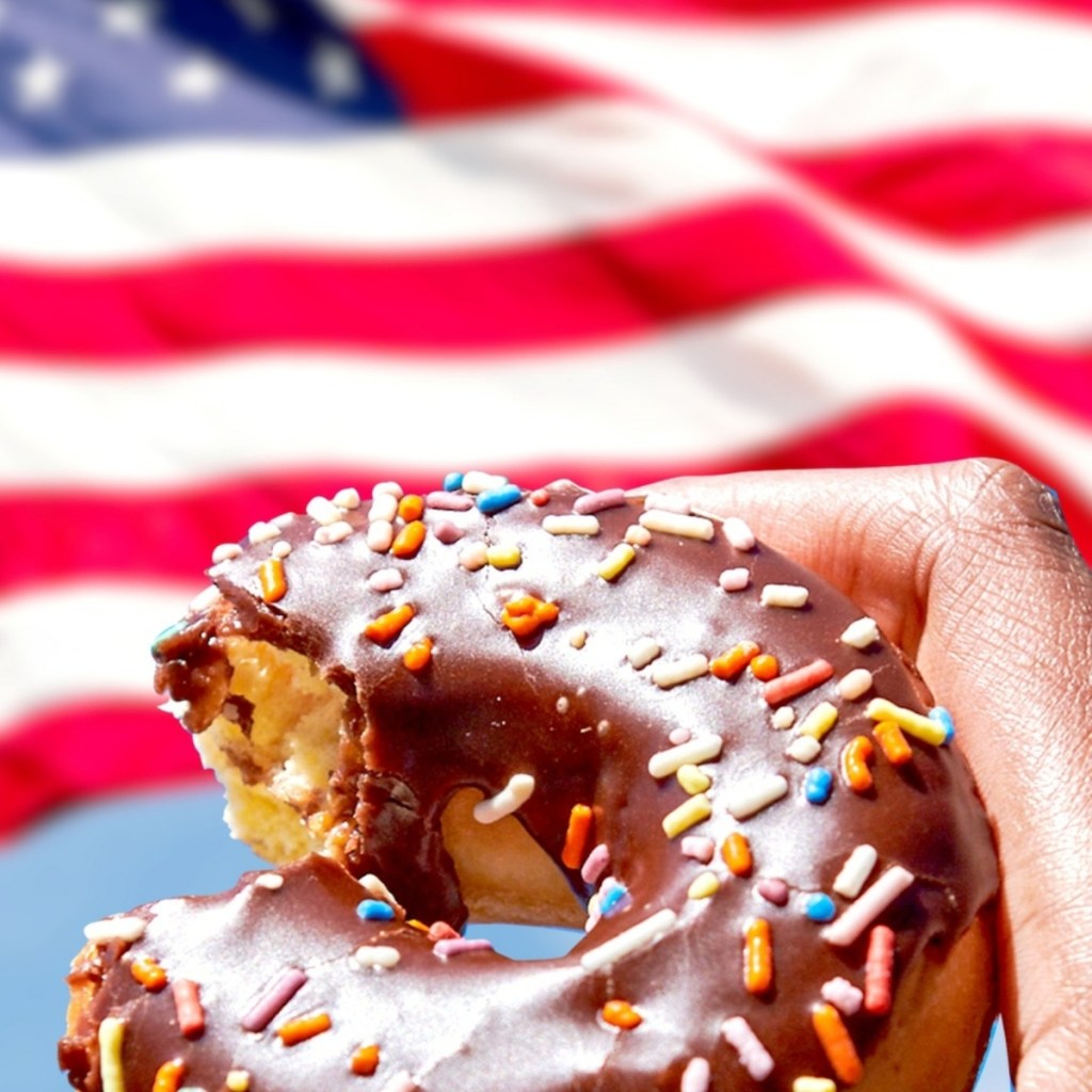 holding a doughnut in front of an American flag