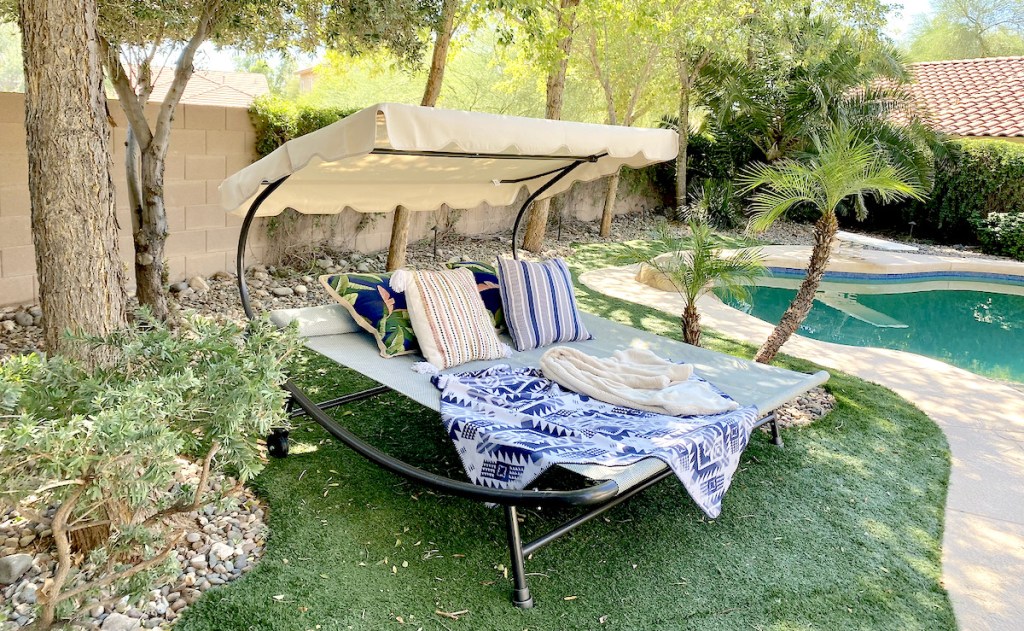 double chaise lounger with blanket and pillows on grass sitting out by pool
