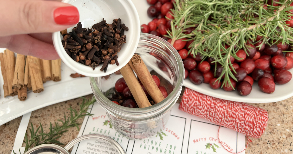 adding cloves to jar of potpourri while making one of our easy diy mason jar gift ideas for christmas