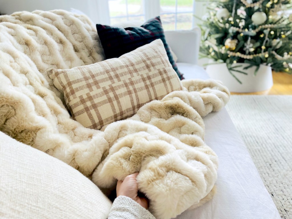 hand holding corner of faux fur throw blanket on couch with pillows