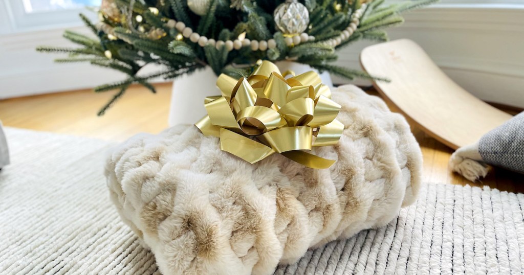 folded faux fur throw blanket with big gold bow on rug under christmas tree