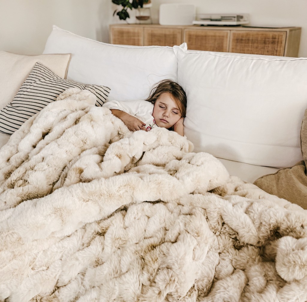 girl laying on couch with beige fur throw blanket