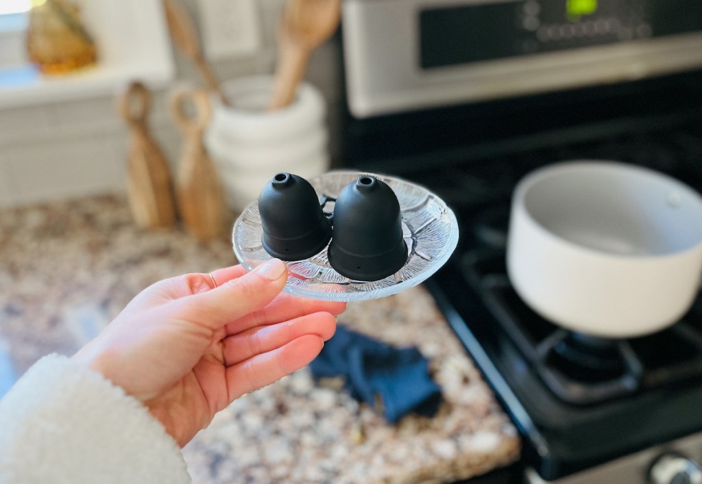 hand holding a clear plate with black menstrual cups on top