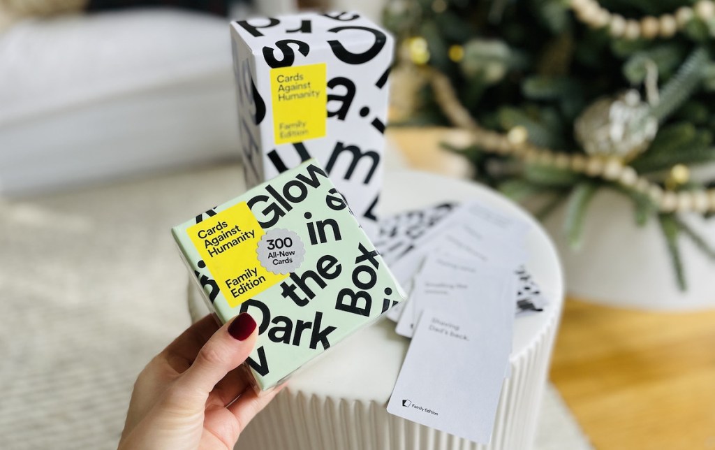 hand holding glow in the dark extension pack with cards against humanity family edition game