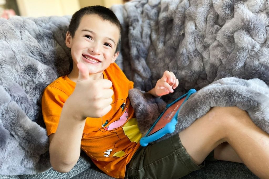 child holding a Contixo tablet and giving a thumbs up