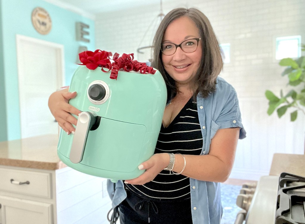 woman holding blue air fryer with red bow standing in kitchen