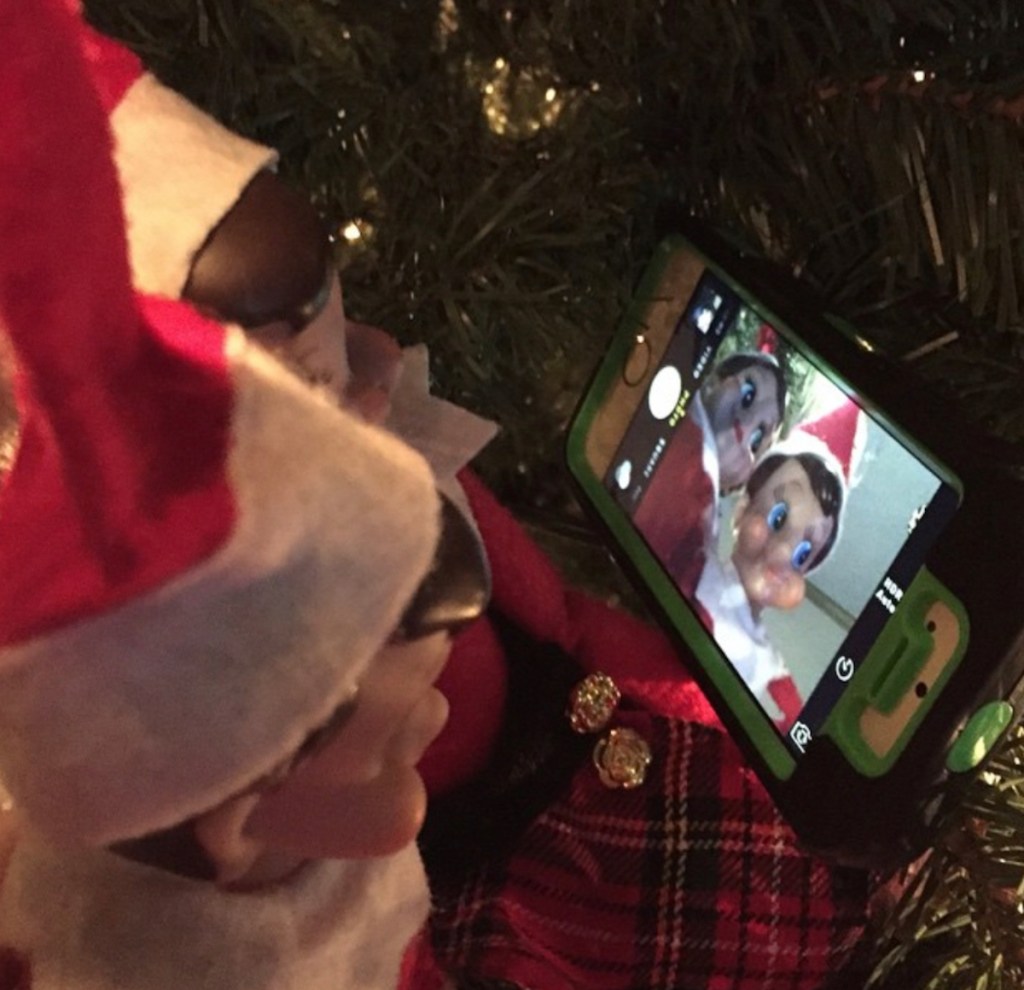 two elves sitting in a christmas tree with phone taking selfie