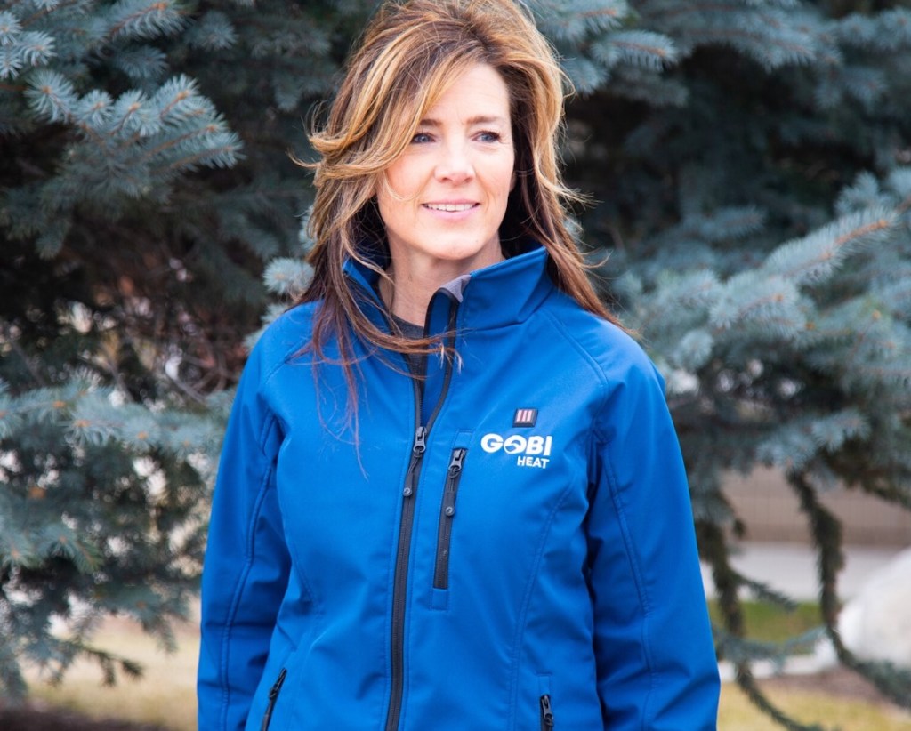 woman standing in front of evergreen trees wearing bright blue jacket
