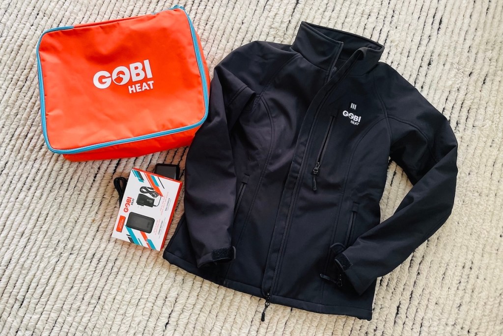 gobi heat black jacket and orange bag laying on rug