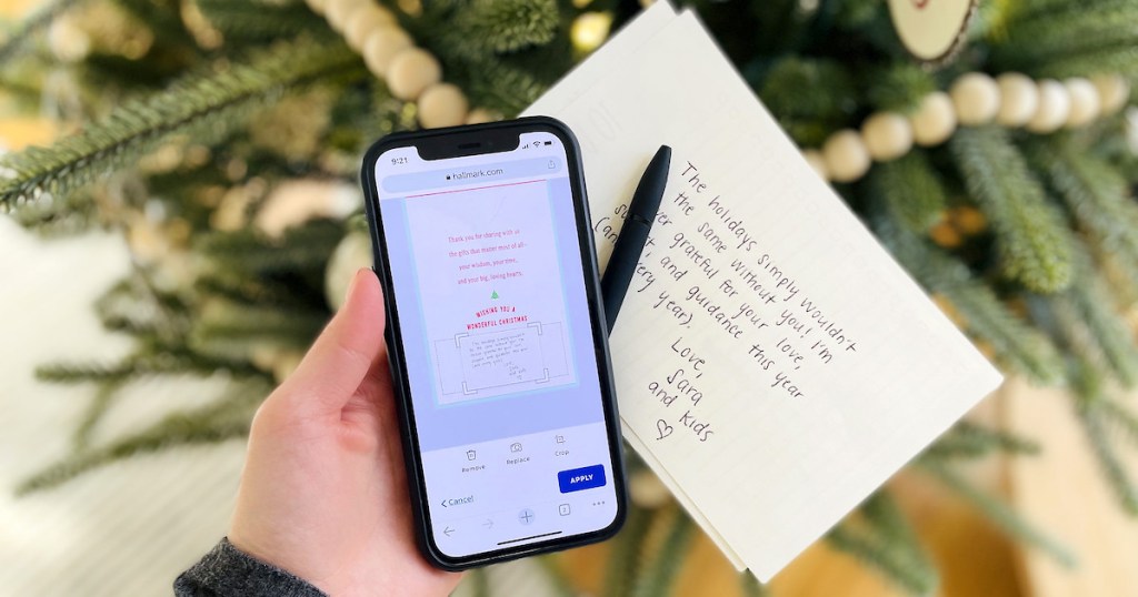 hand holding phone with handwritten note on paper in front of christmas tree