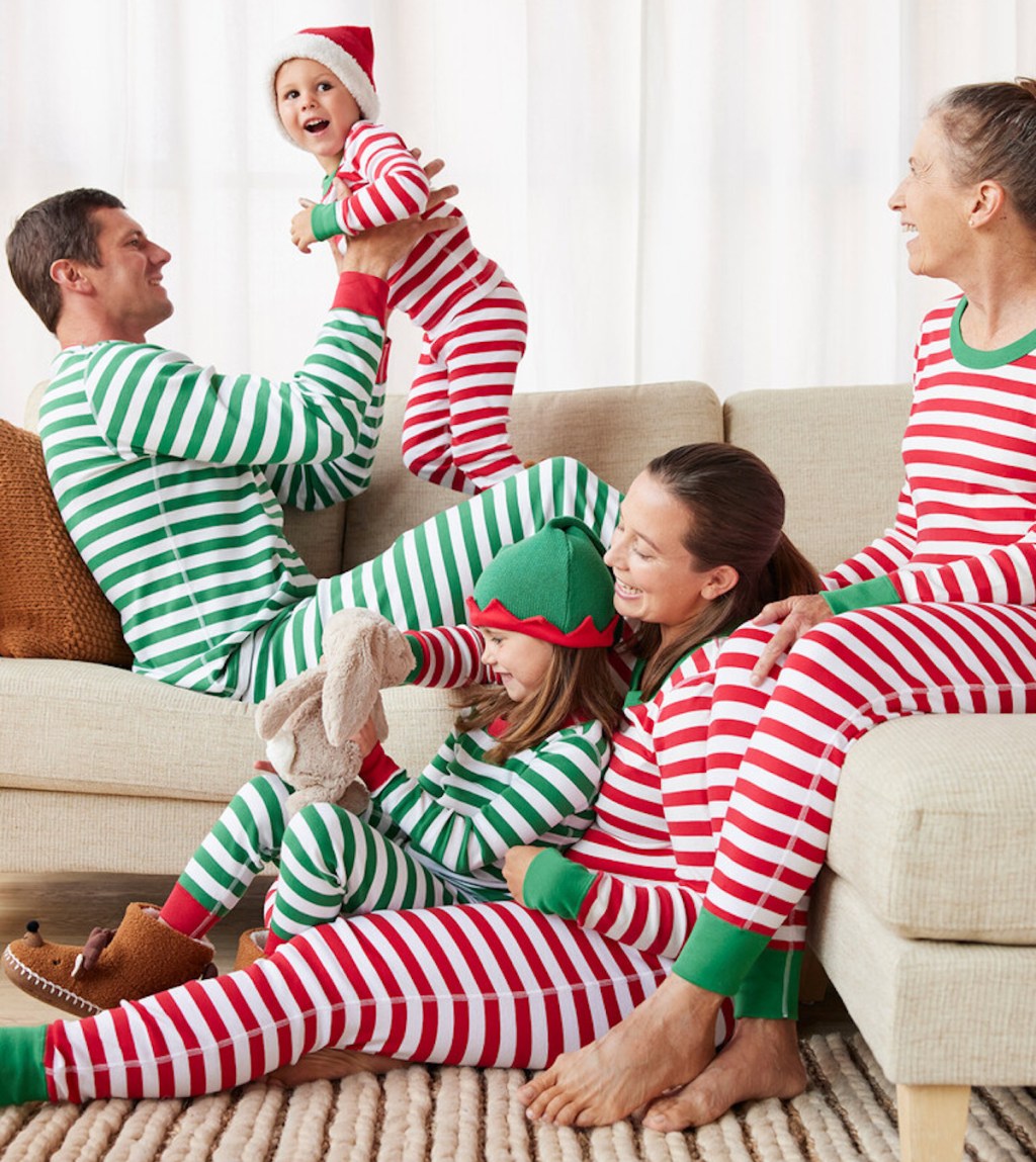 family playing and smiling on couch and floor wearing green and red stripe matching pajamas