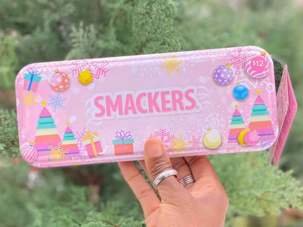 hand holding up pink tin in front of tree containing lip balms