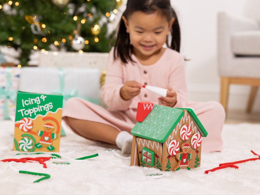 little girl playing with a melissa & doug gingerbread house in front of a Christmas tree