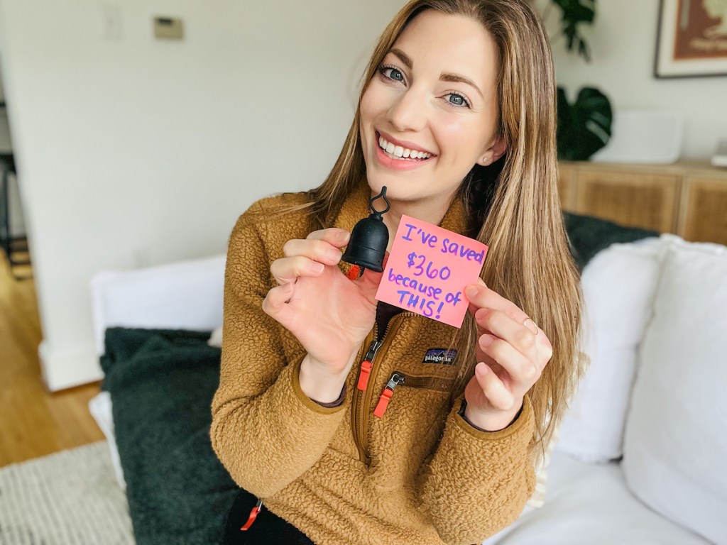 woman holding menstrual cup and pink post it note with savings