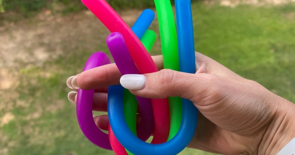 hand holding colorful noodle toys outside in front of grass