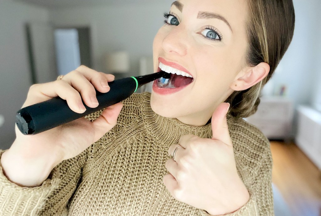 woman brushing teeth with oral b io series 8 toothbrush giving thumbs up