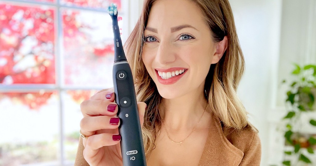 woman holding oral b io series 8 toothbrush in hand smiling