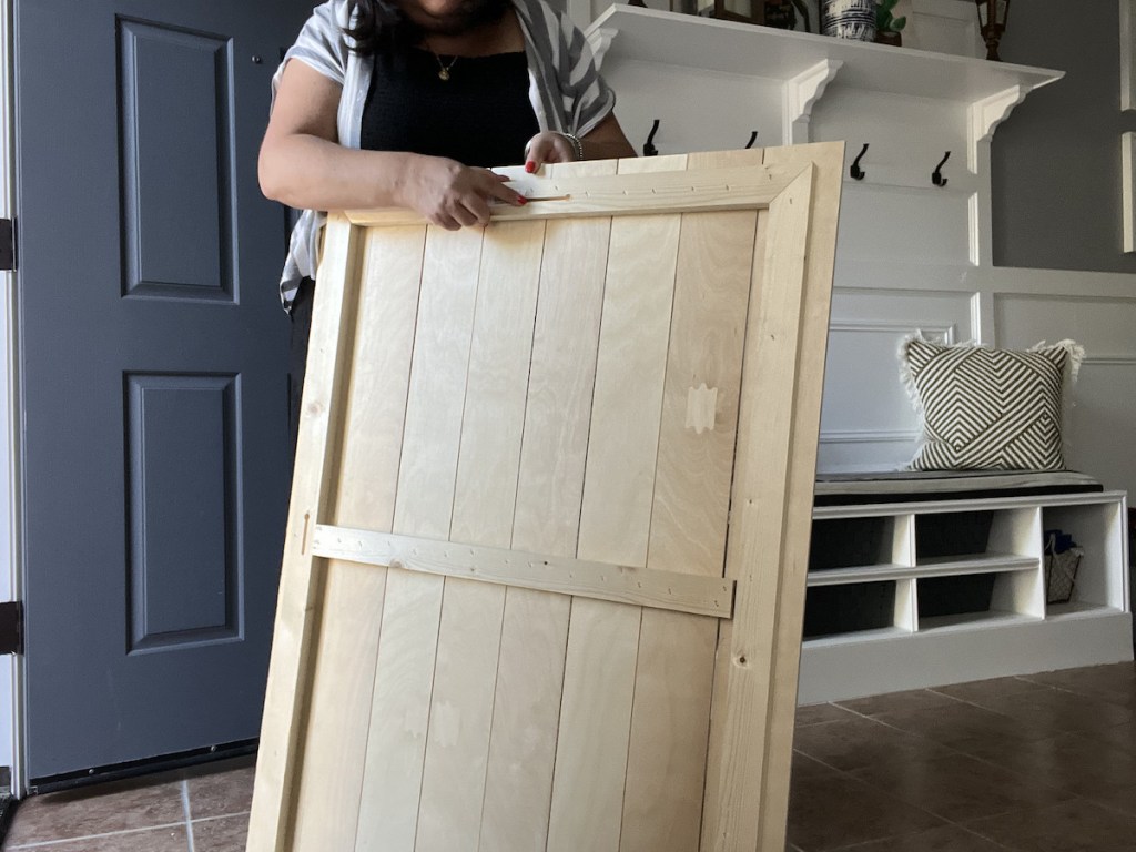 woman holding large wood pallet board frame in entryway