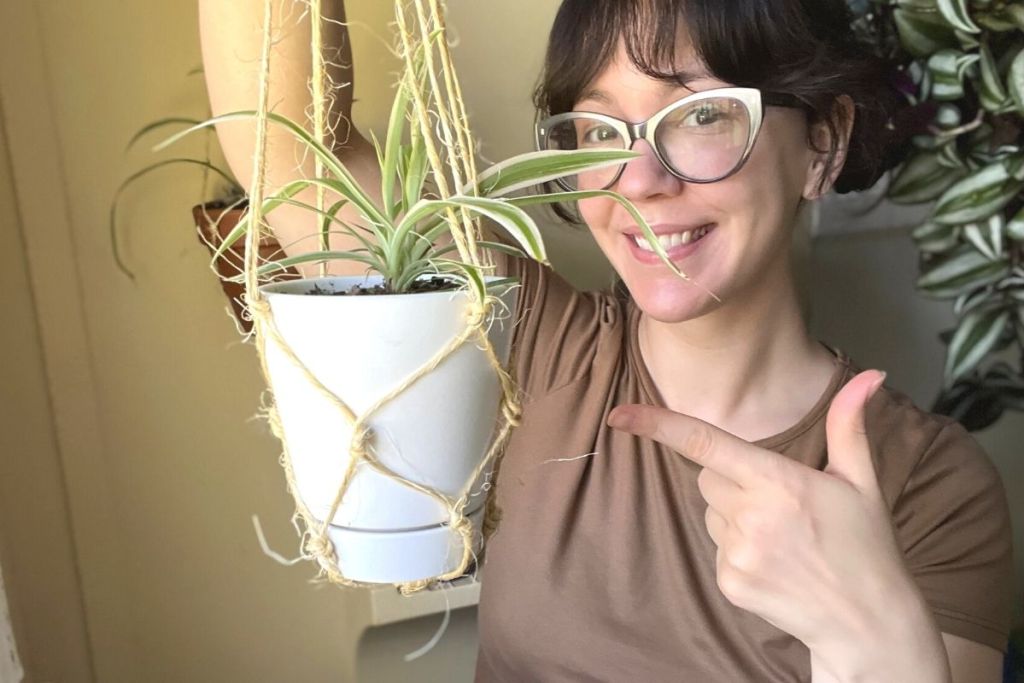 woman holding and pointing to potted plant in macrame hanger
