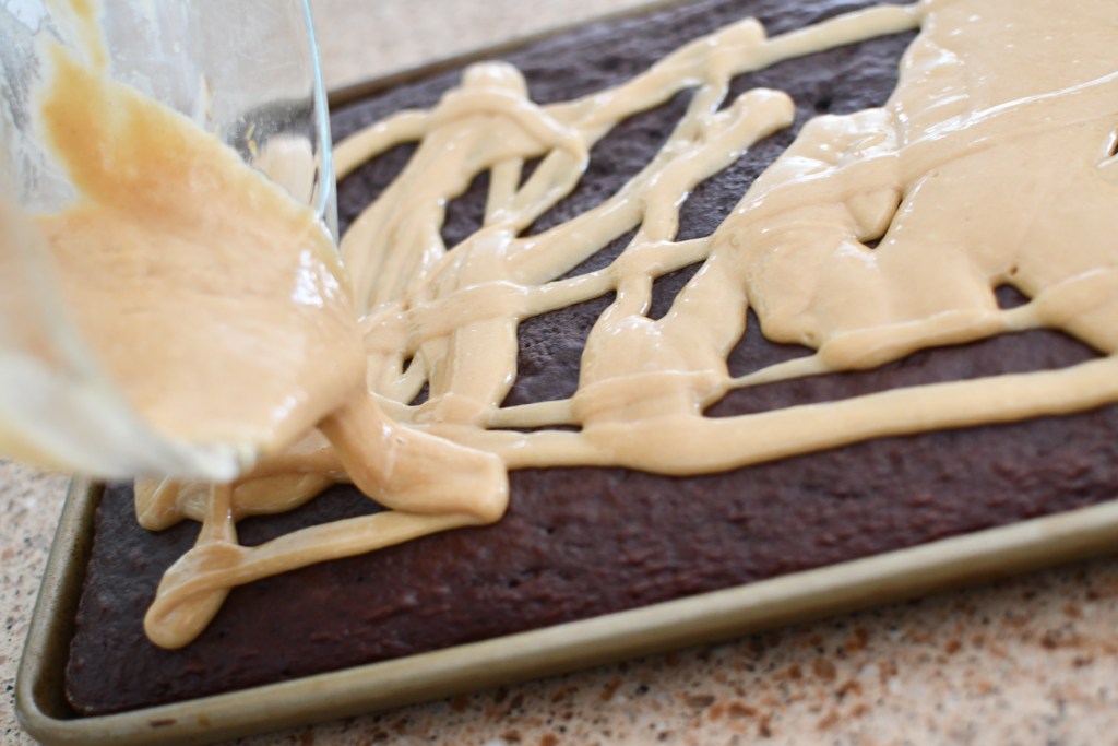 pouring peanut butter glaze over sheet cake