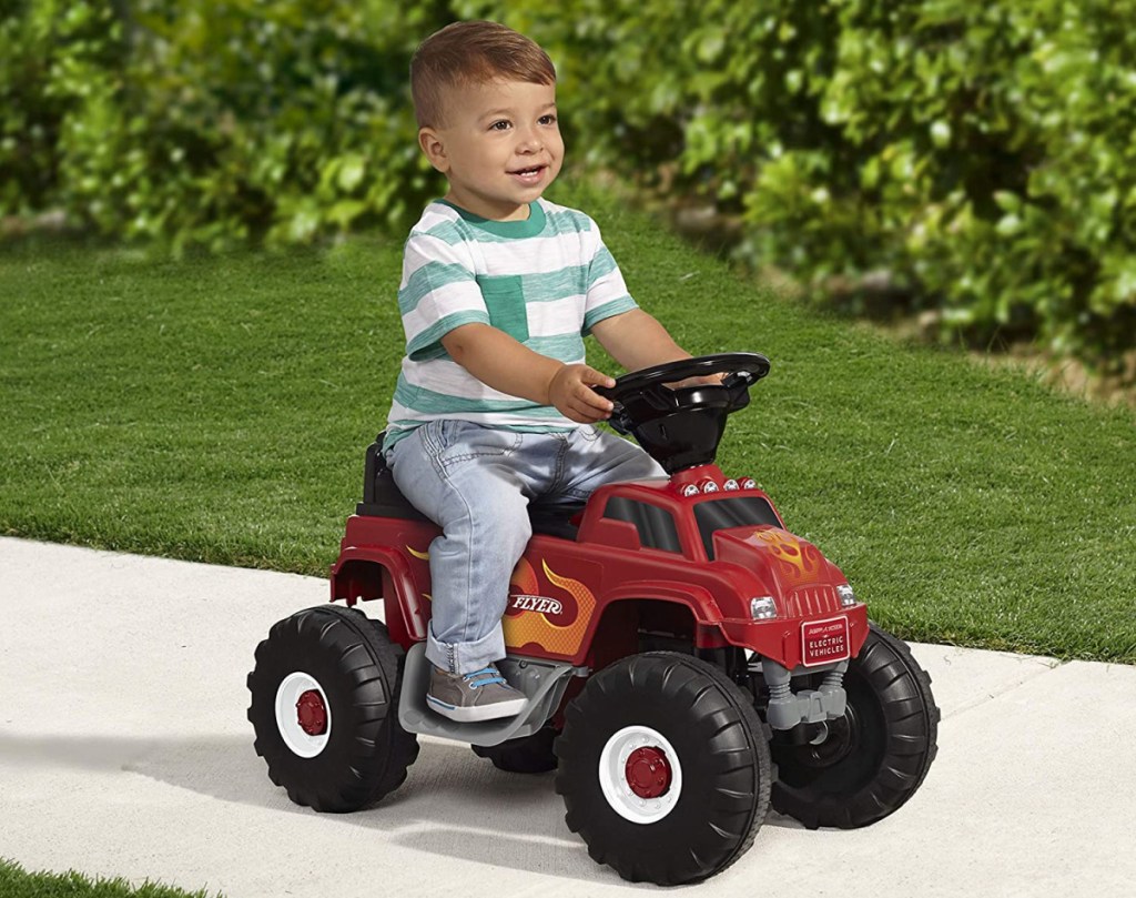 boy riding a radio flyer monster truck ride on toy along a path near grass and trees